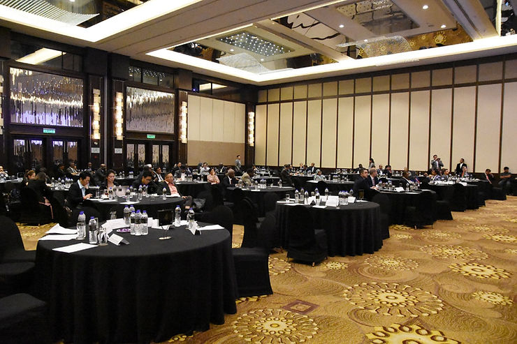 Spacious ballroom with round tables, attendees seated, black tablecloths, papers, and water bottles